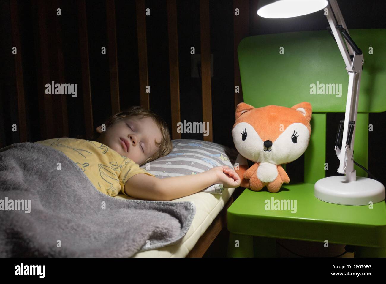 Little boy sleeps in a crib under the light of a night lamp Stock Photo