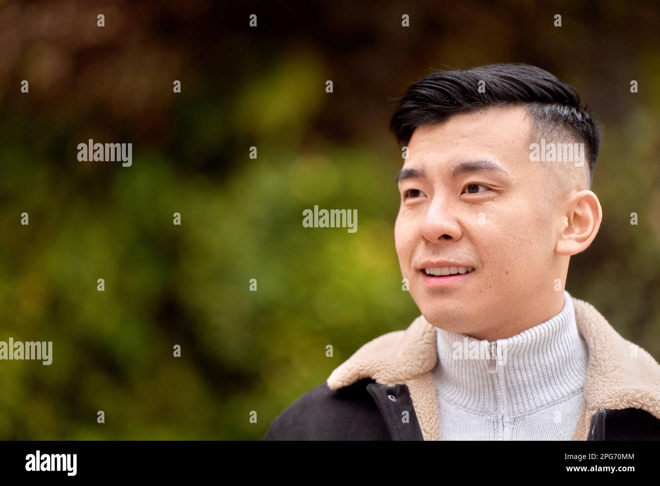 Attractive Asian man looking to the side smiling while relaxing outdoors in a park.  Stock Photo