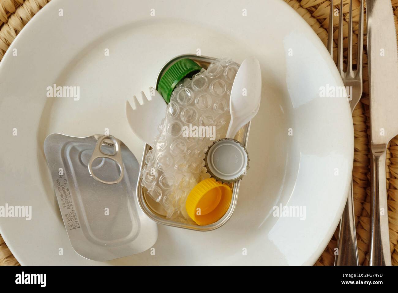 Aluminium Tuna can full of plastic trash on white plate - Concept of ecology and plastic pollution Stock Photo
