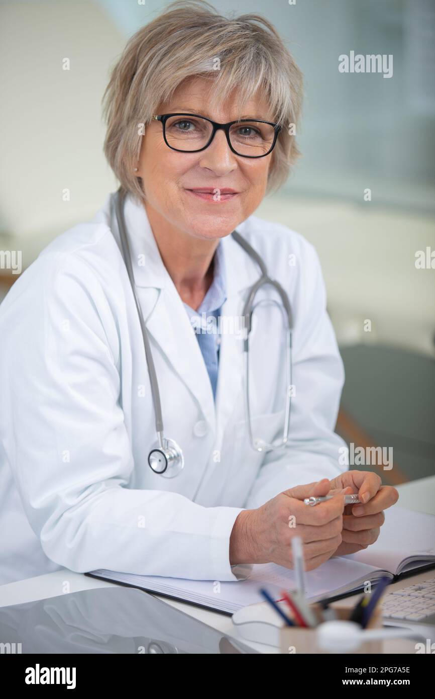smiling attractive mature female doctor sat at her desk Stock Photo - Alamy
