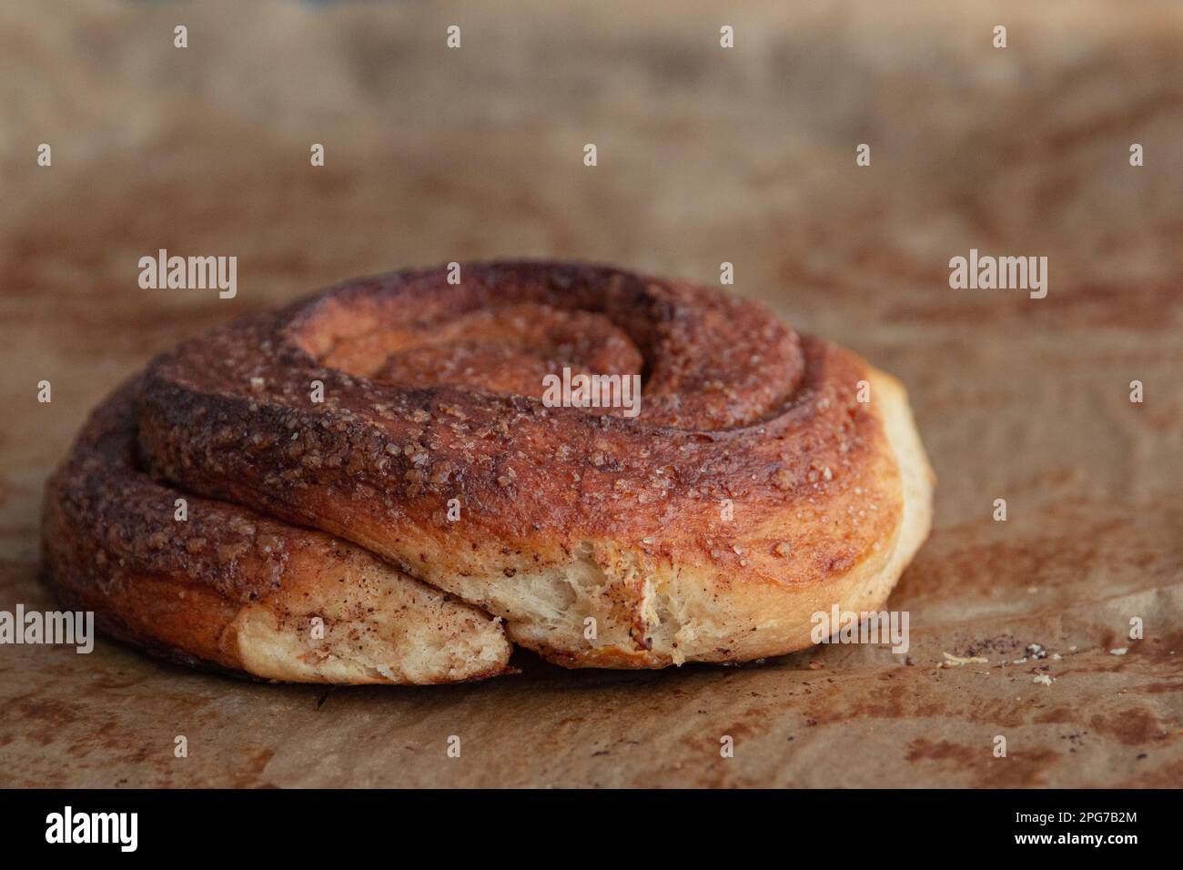 side view of homemade cinnamon bun on sheet of baking paper. Photographed with shallow depth of field. Stock Photo