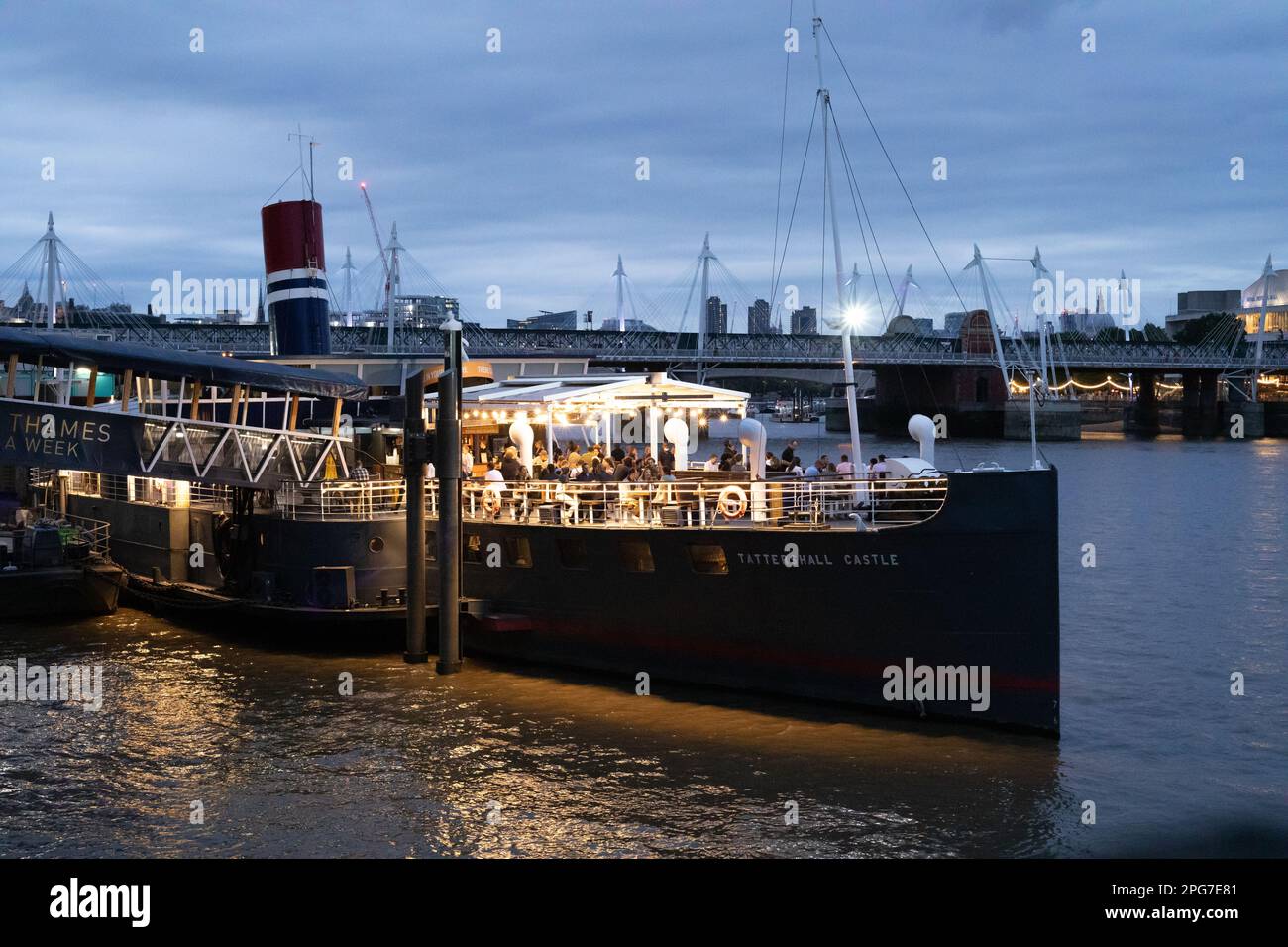 The Tattershall Castle boat is moored on the side of the river Thames at Victoria Embankment and is entertaining crowds of people in the evening. Stock Photo