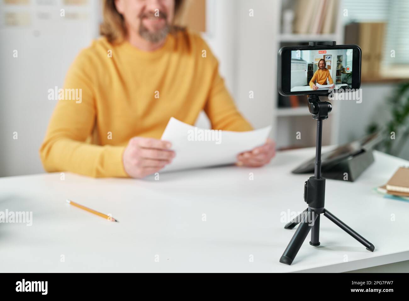 Selective focus of smartphone standing on tripod on table with teacher having online lesson Stock Photo
