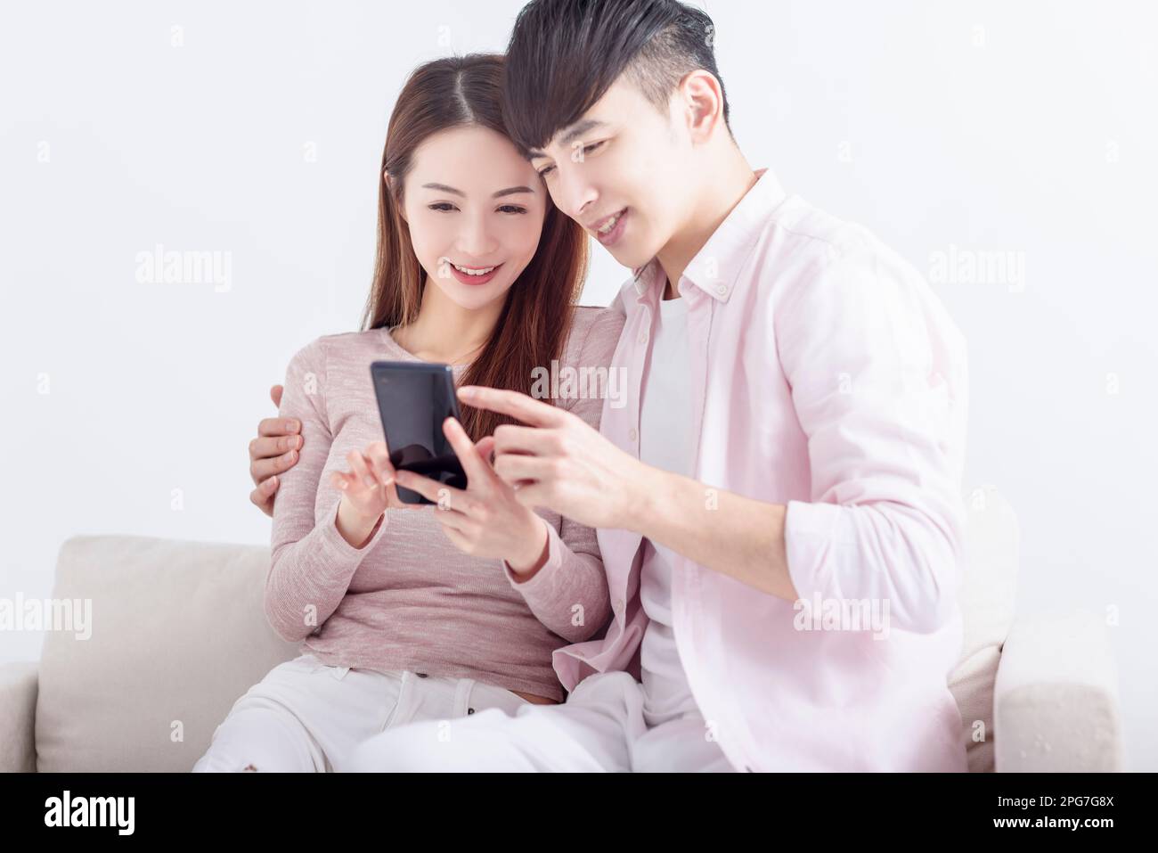 Young  couple using smart phone , browsing internet, chatting online, relaxing on sofa at home Stock Photo