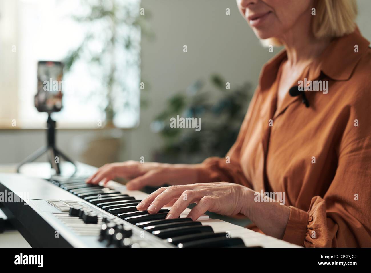 Mature teacher playing on piano online and recording her lesson on professional camera for students Stock Photo