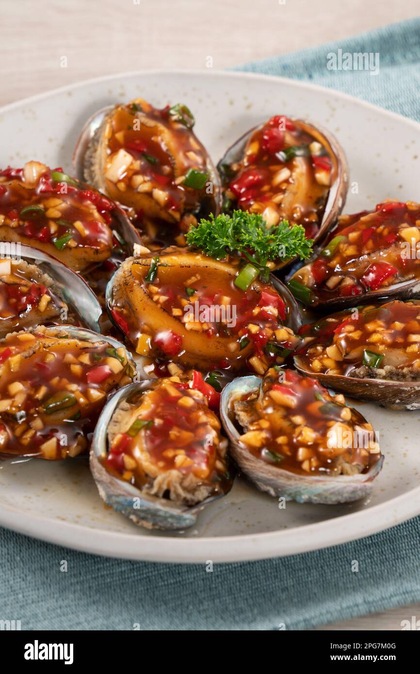 Delicious steamed abalone with spicy tomato sauce, Taiwanese five flavor sauce on wooden table background. Stock Photo