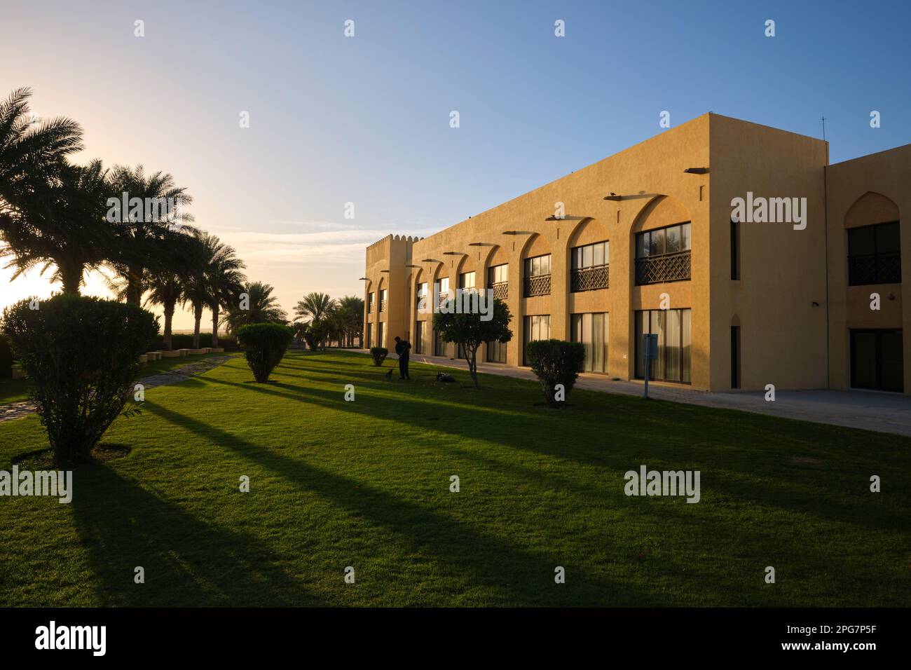 Morning sunrise on the hotel building grounds. A worker grooms the lawn. At the Tilal Liwa Hotel desert vacation resort near Abu Dhabi, UAE, United Ar Stock Photo