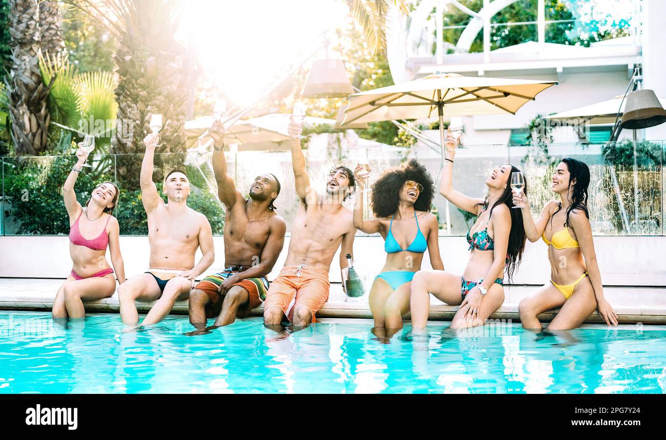 Front view of friends group cheering at exclusive hotel swimming pool wearing swim cloth - Summer life style concept with young people having fun Stock Photo