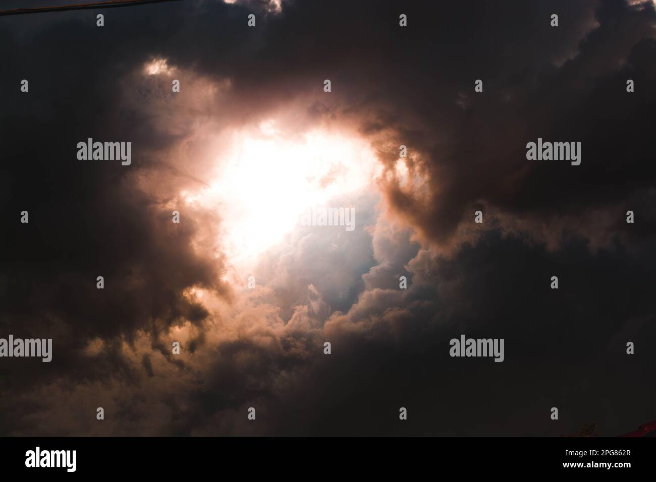 A dramatic sky of roiling dark clouds illuminated by a warm golden ...