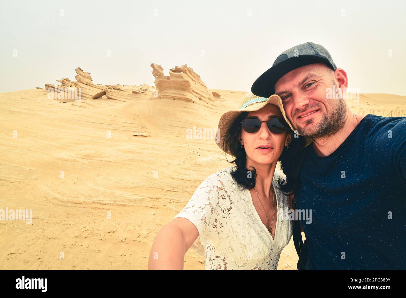Multiracial couple taking selfie at fossil desert in Abu Dhabi, UAE. Fun time together concept alternative fashion travelers, multi-ethnic boyfriend a Stock Photo