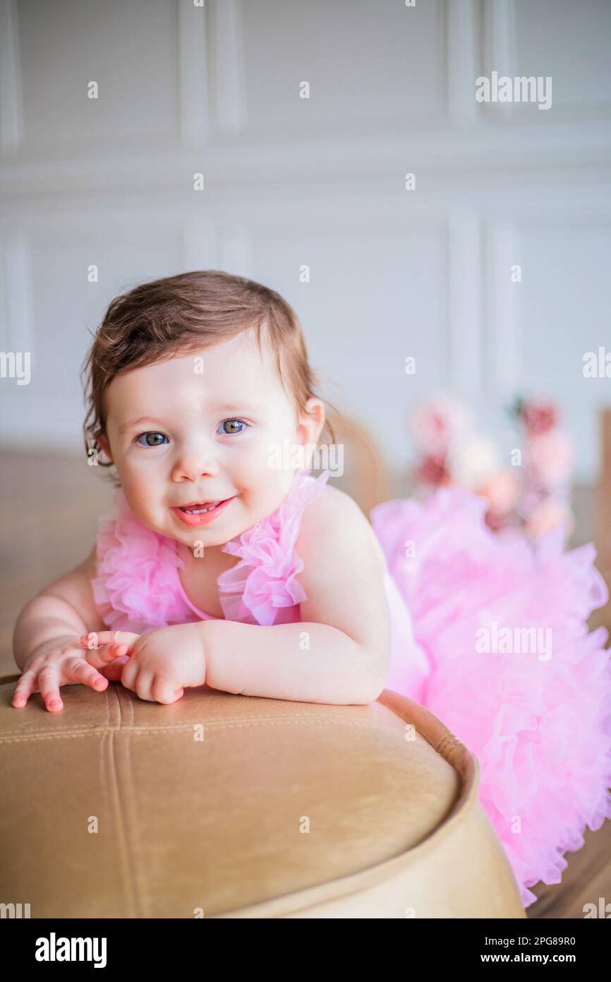A baby girl in a pink dress laying on a chair, beaming a sweet smile at ...