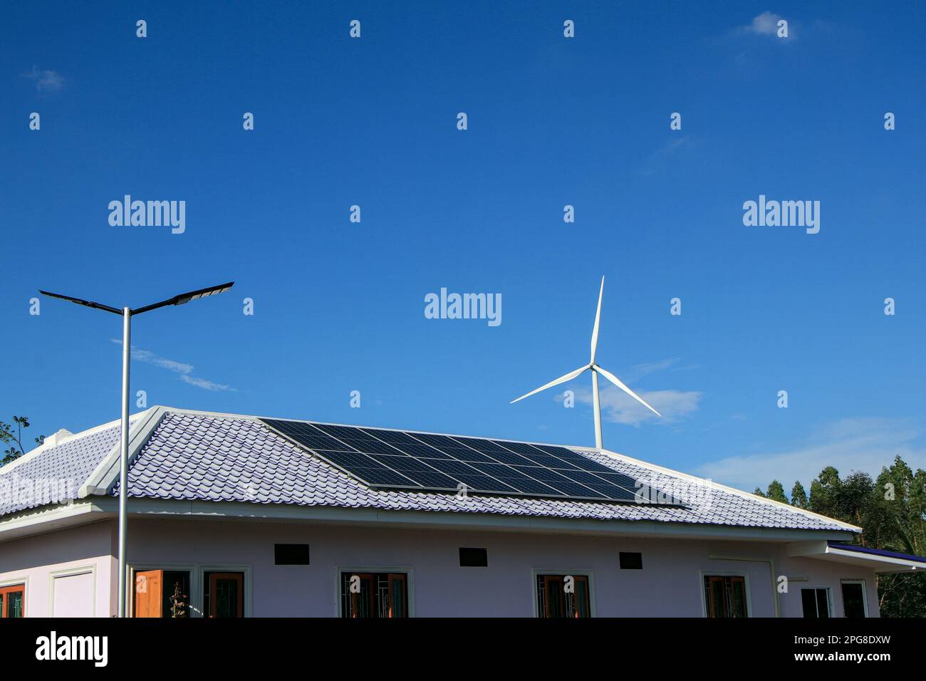 Solar panels on the roof and there are also wind turbines around. The concept of renewable and sustainable resources. Stock Photo