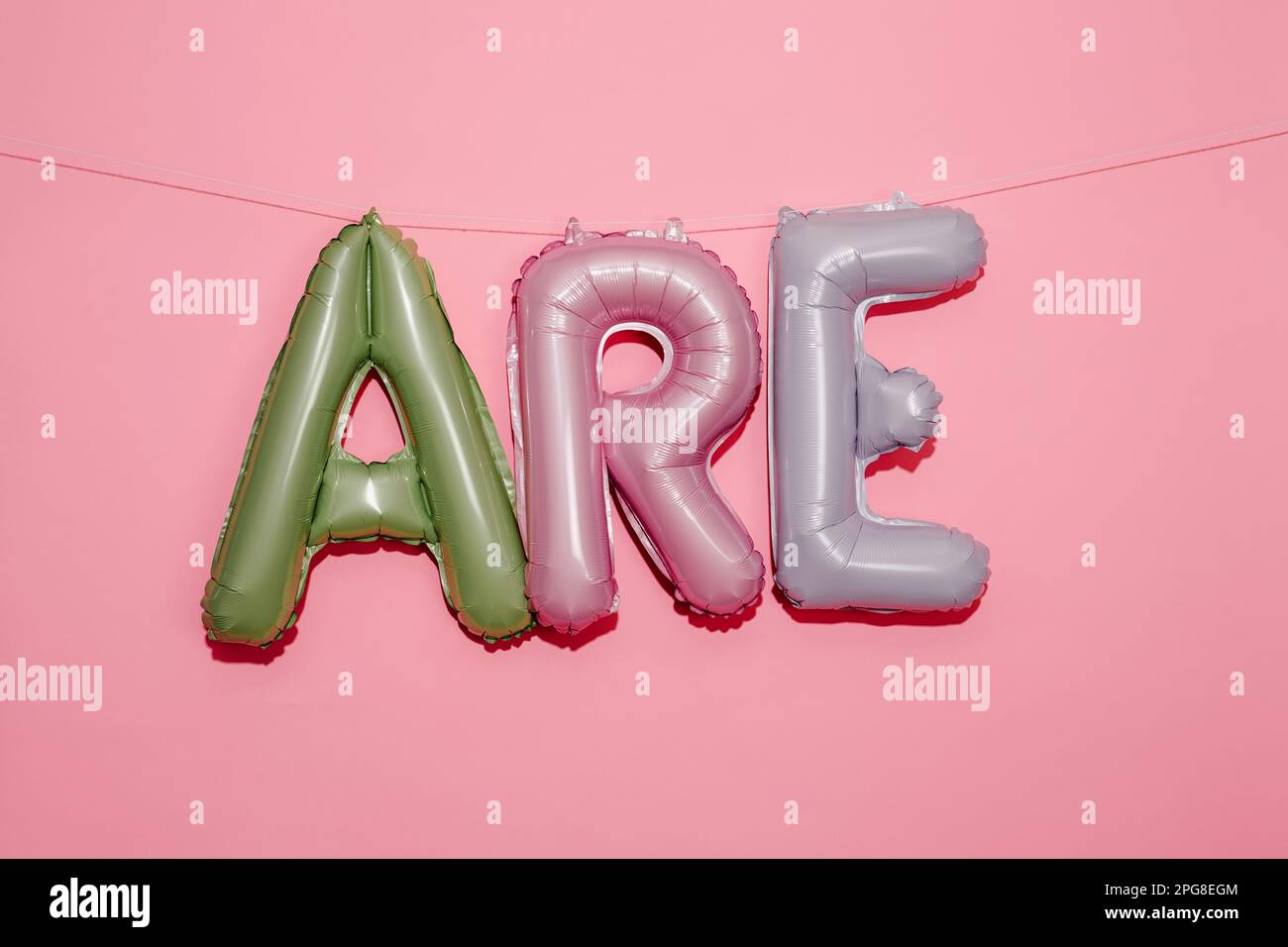 alphabet-shaped balloons of different colors forming the text are hanging from a string on a pink background with some blank space on top Stock Photo