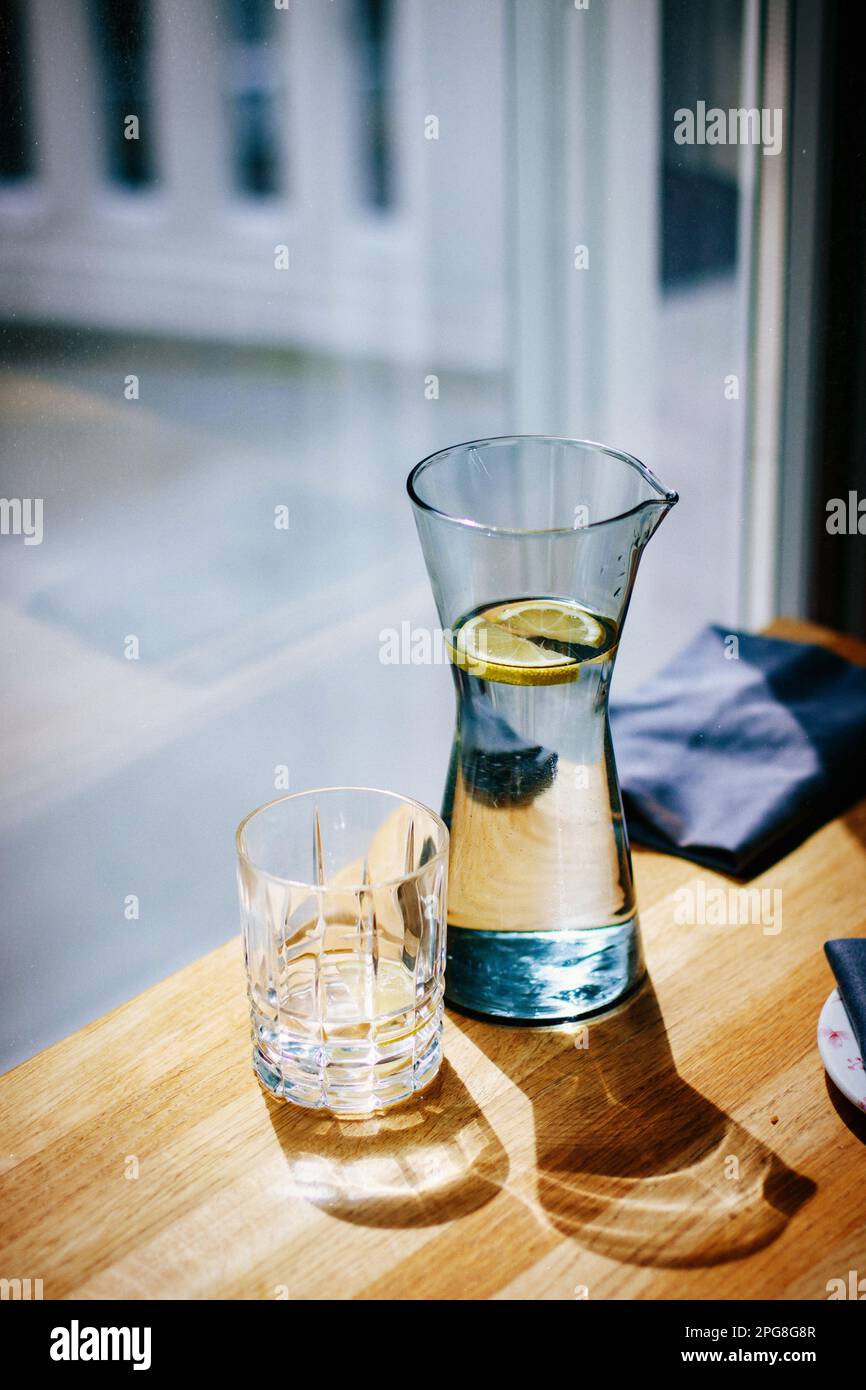 A glass jug on a table filled with a cool, refreshing beverage, with a lemon slice. Stock Photo