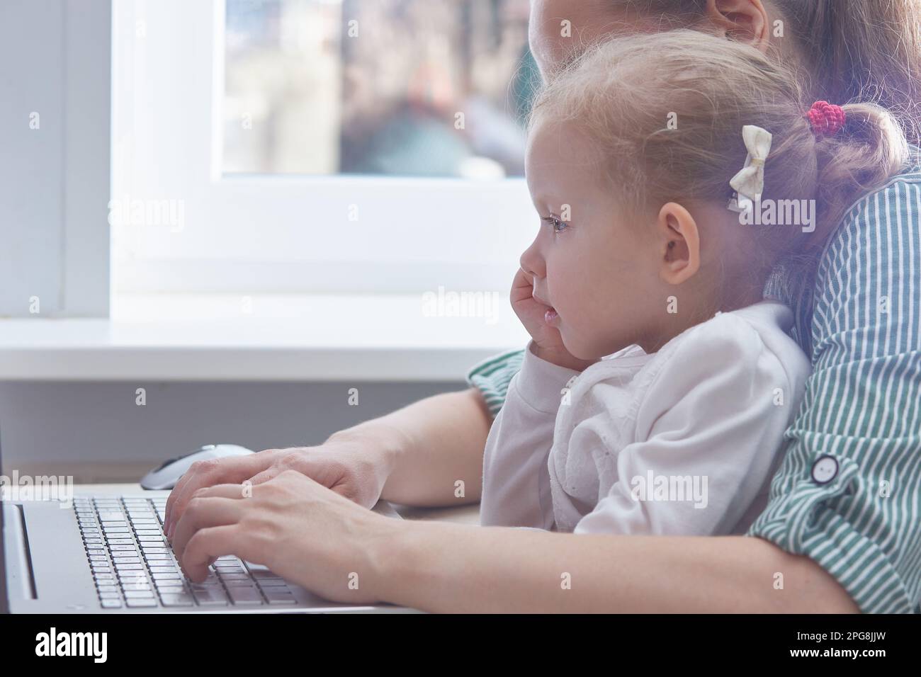 The child is in the arms of a mother working on a laptop at home. The concept of freelancing and working from home with children. Copy space. Stock Photo