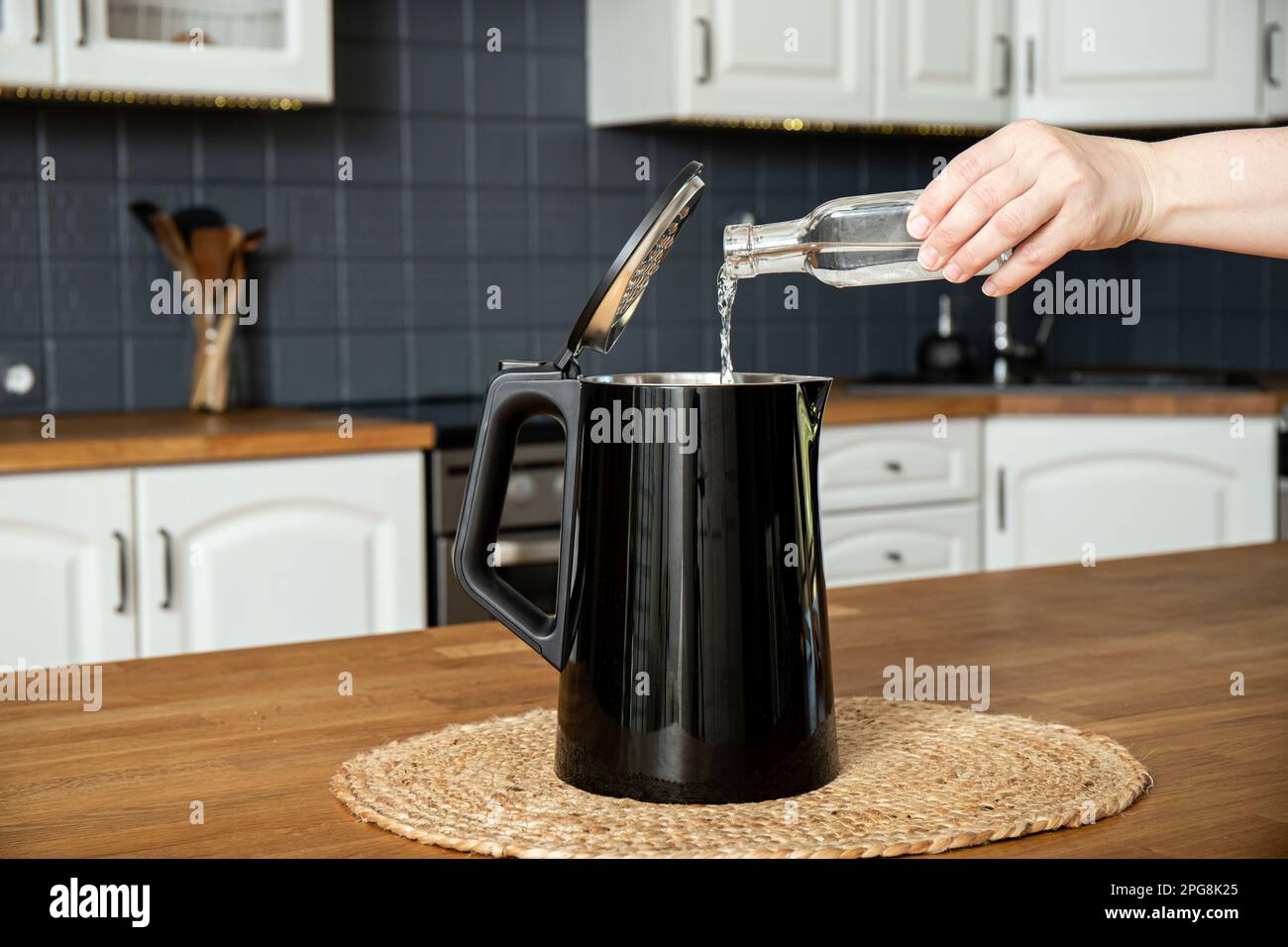Woman pouring natural destilled acid white vinegar in electric kettle to remove boil away the limescale. Descaling a kettle, remove scale concept. Stock Photo
