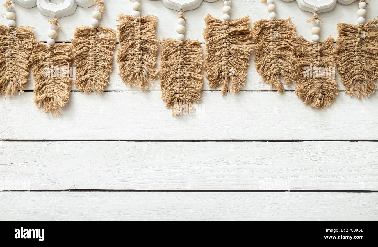 Light brown leaf or feather shape macrame hanging against white wood board background in home room. Lot of copy space, boho background. Stock Photo