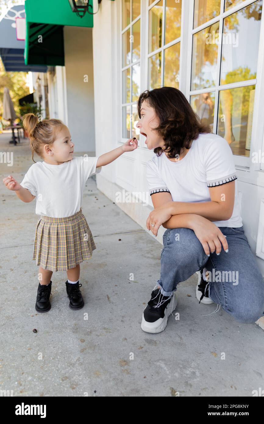 toddler girl in skirt and t-shirt holding acorn near mother with opened mouth,stock image Stock Photo