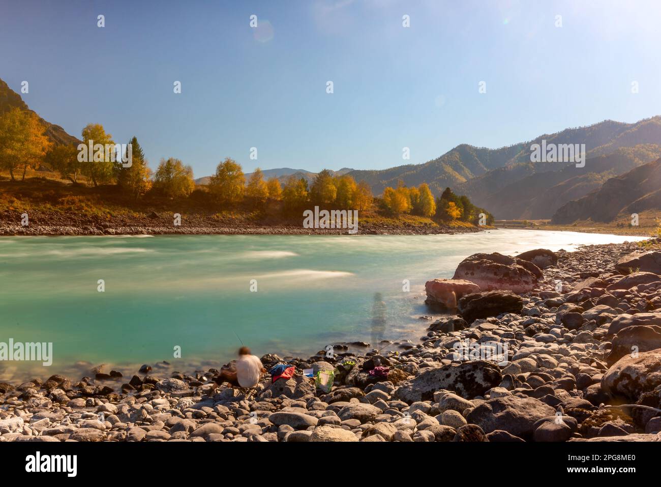 Blurred silhouettes of two women resting with a fishing rod on the bank of the mountain river Katun between rocks in the afternoon in autumn. Long exp Stock Photo