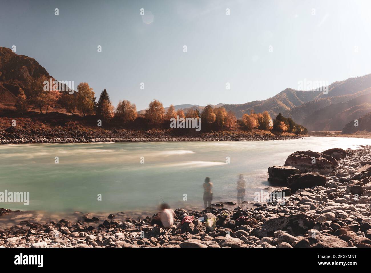 Blurred silhouettes of two women resting with a fishing rod on the bank of the mountain river Katun in Altai between the rocks in the afternoon in aut Stock Photo
