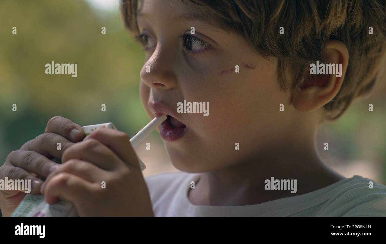 Portrait of a child drinking juice from straw from carton box outside
