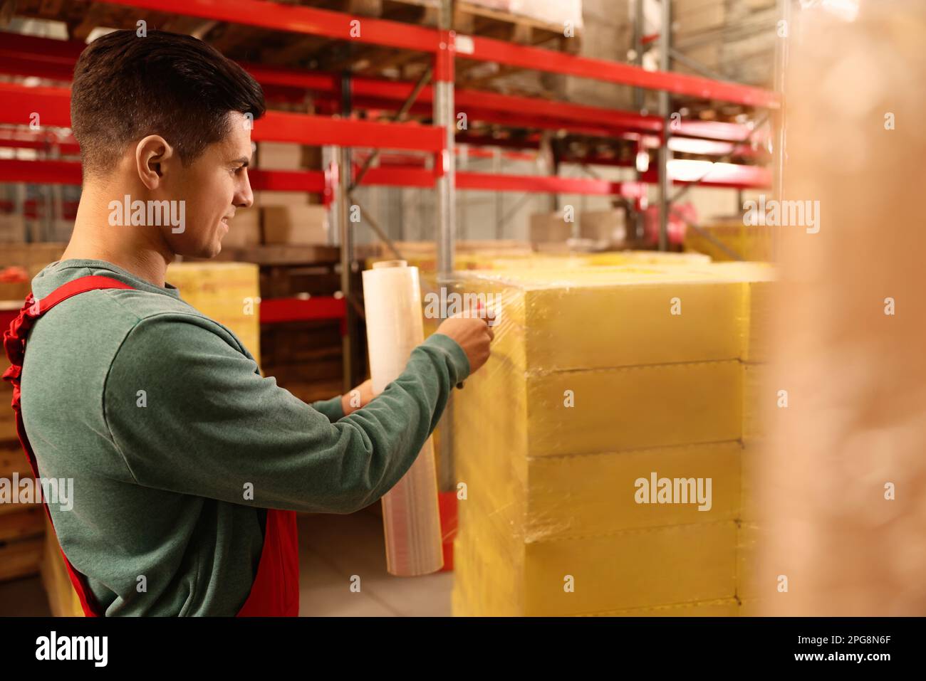 Worker wrapping boxes in stretch film at warehouse Stock Photo