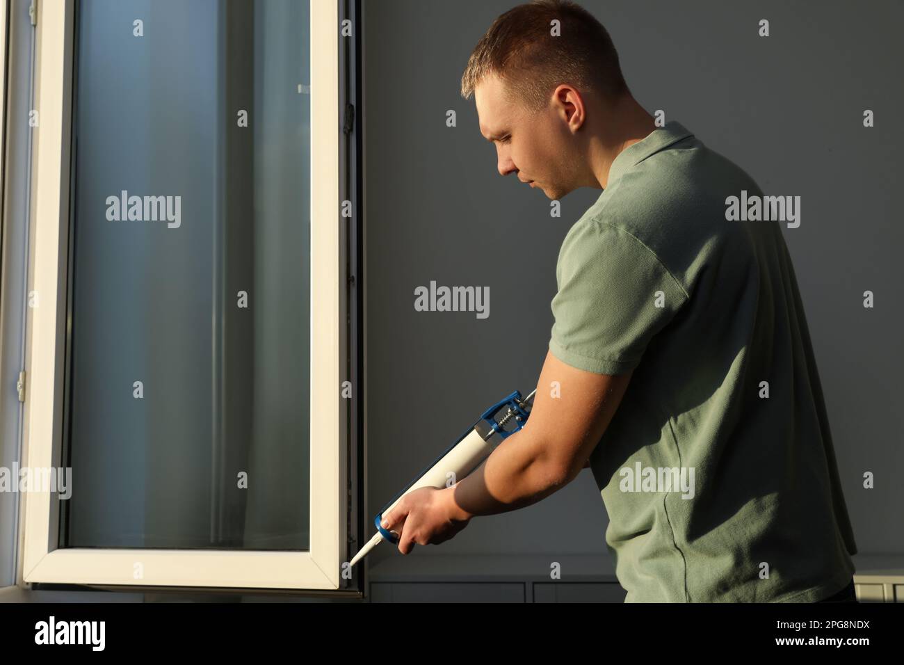 Construction worker sealing window with caulk indoors Stock Photo