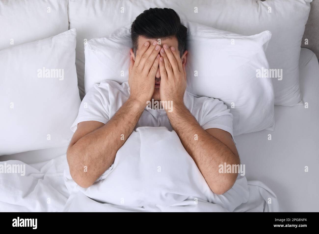 Man covering his face with hands while lying in bed at home, top view