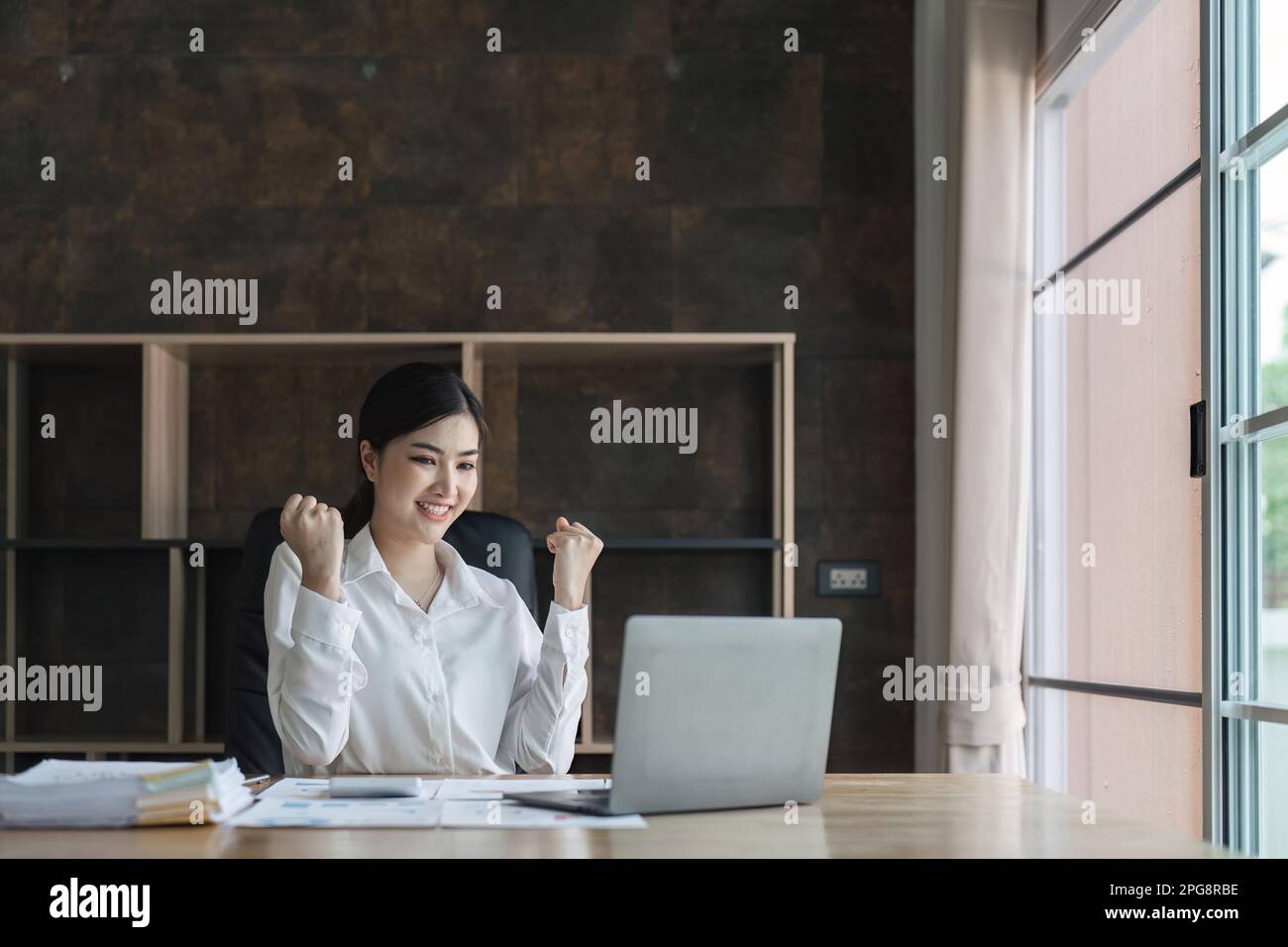 Excited young asian woman sitting at table with laptop and celebrating ...