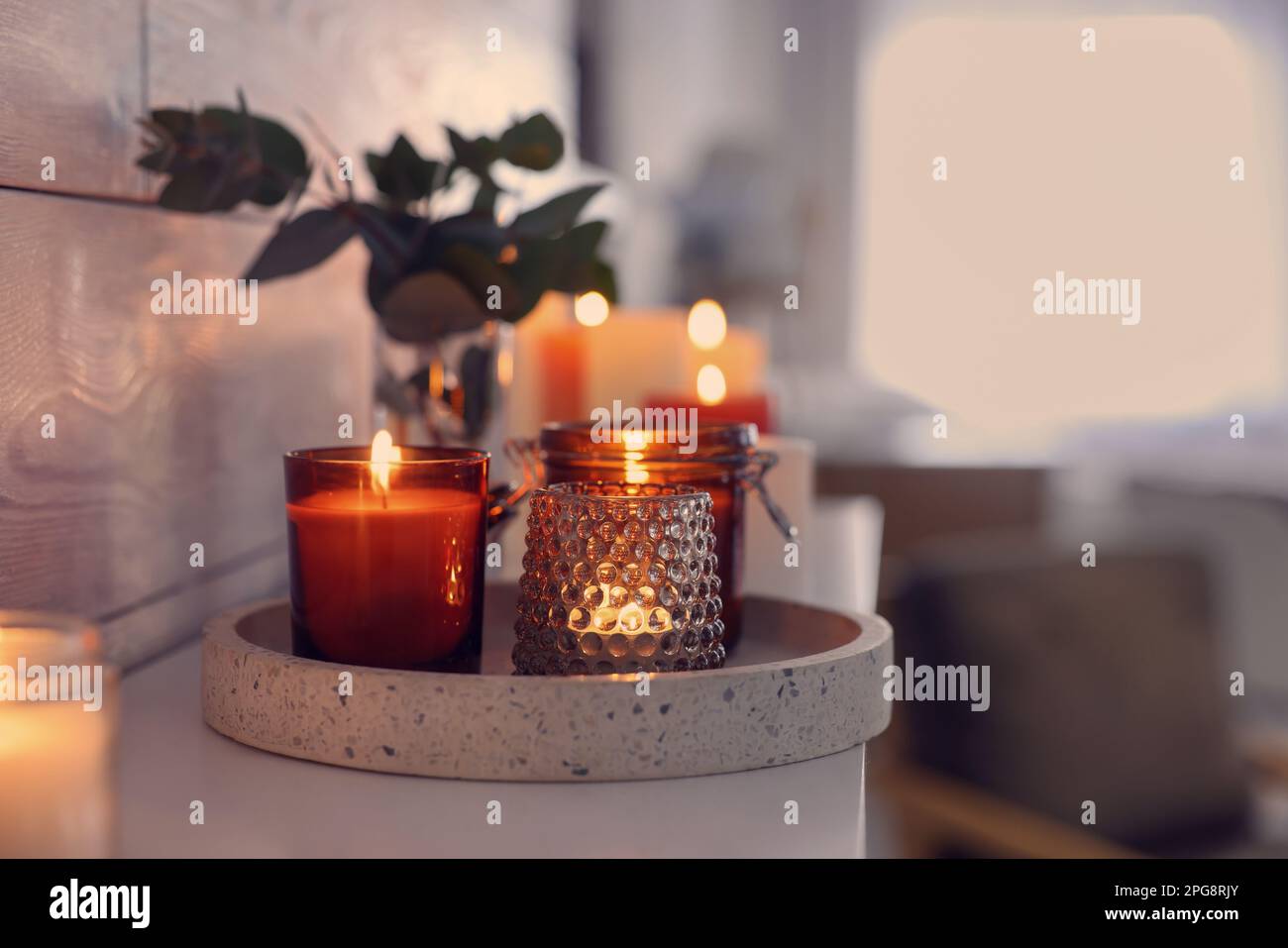 Burning candles on mantel near white wall indoors, space for text Stock