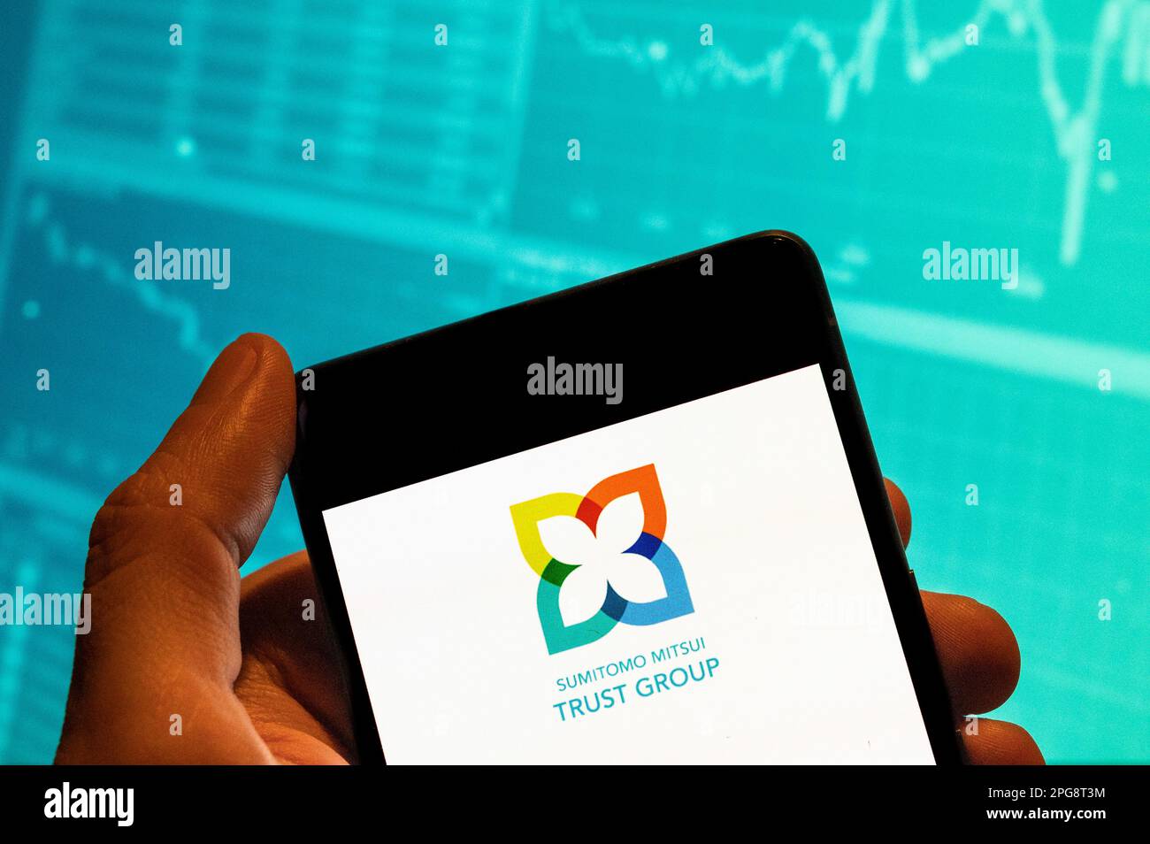 In this photo illustration, the Sumitomo Mitsui Trust Group logo seen displayed on a smartphone with an economic stock exchange index graph in the background. Stock Photo