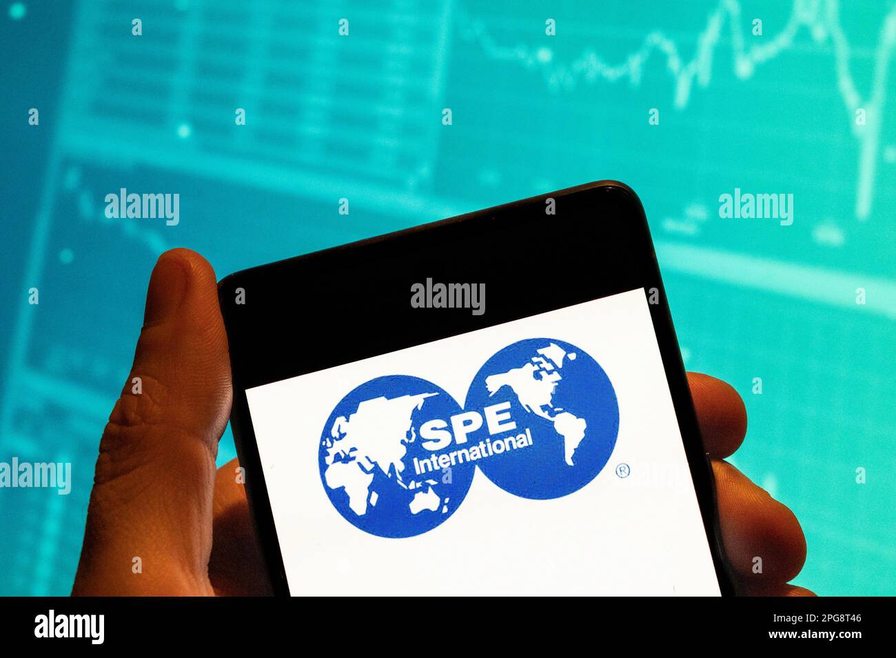 In this photo illustration, the Society of Petroleum Engineers (SPE) logo seen displayed on a smartphone with an economic stock exchange index graph in the background. Stock Photo