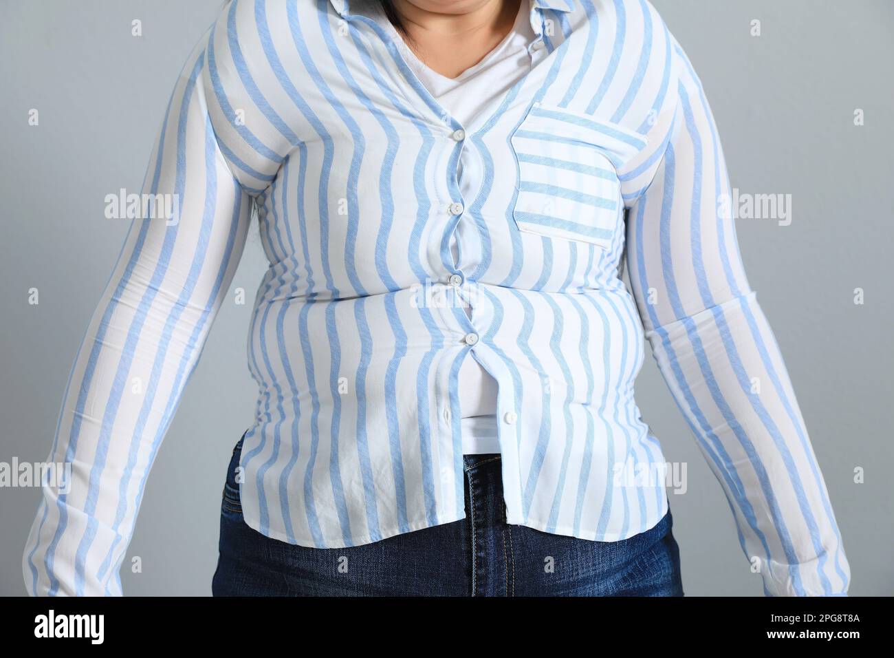 Overweight woman in tight shirt on light grey background, closeup