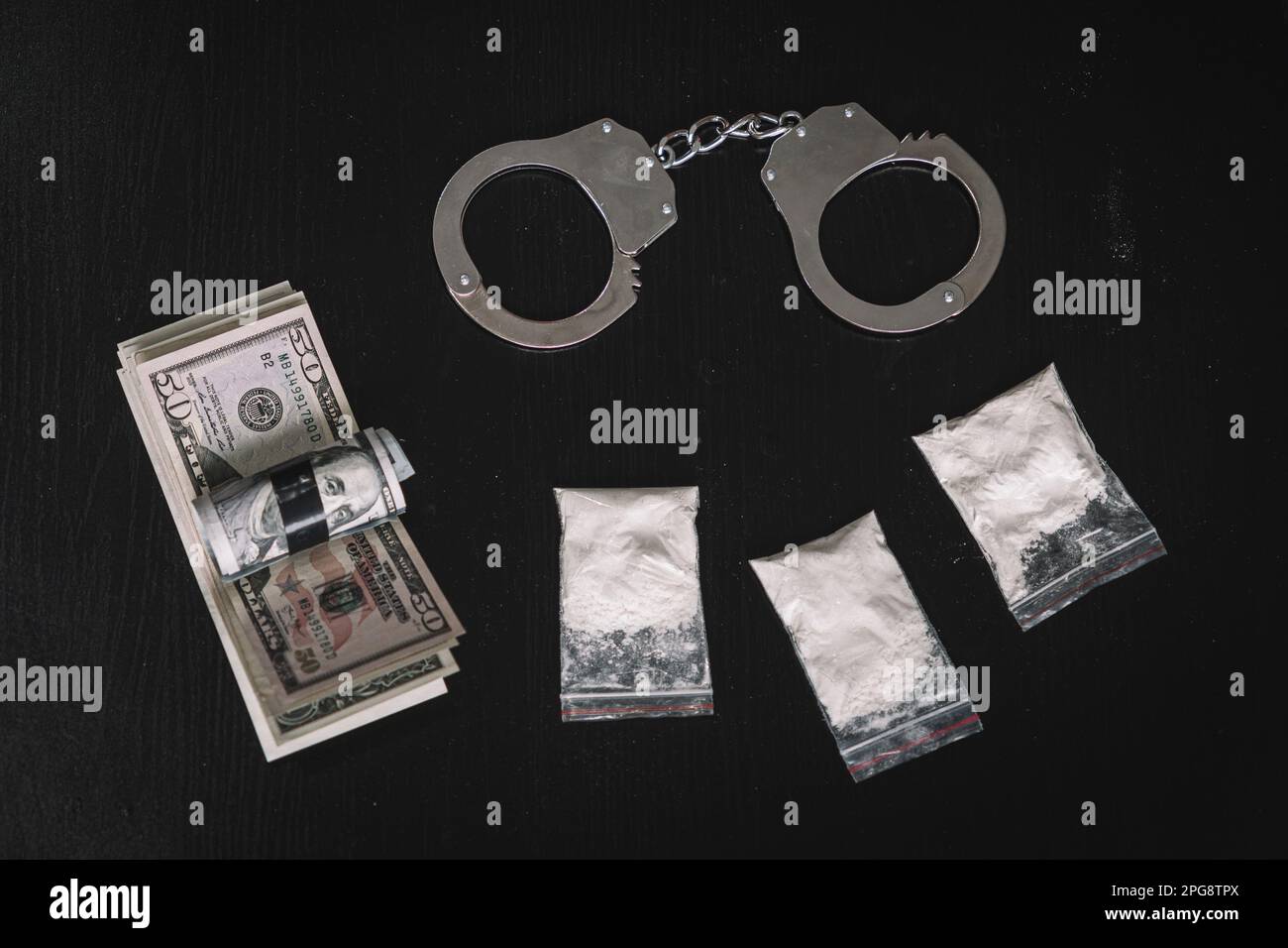 narcotic powder in a bag of money and handcuffs on a black background of the table. The concept of drug trafficking or drug trafficking. Stock Photo