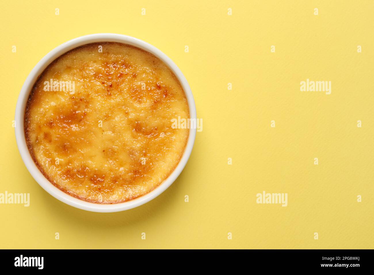 Delicious creme brulee in ceramic ramekin on yellow background, top