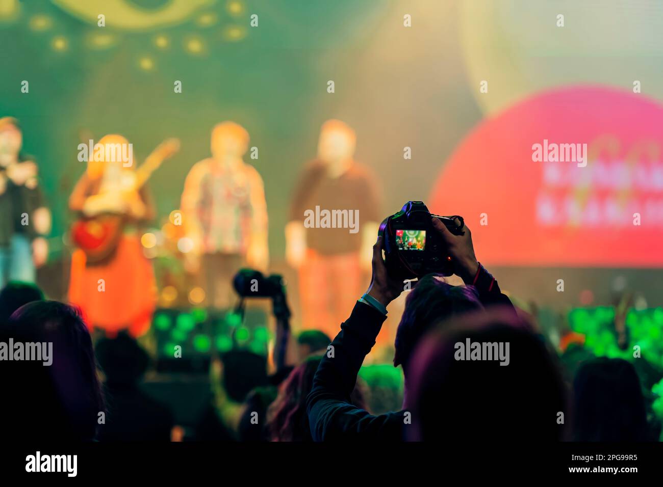 Silhouette of spectator, photographer taking picture with camera at concert with crowd people. Bright colorful light by stage lights Stock Photo