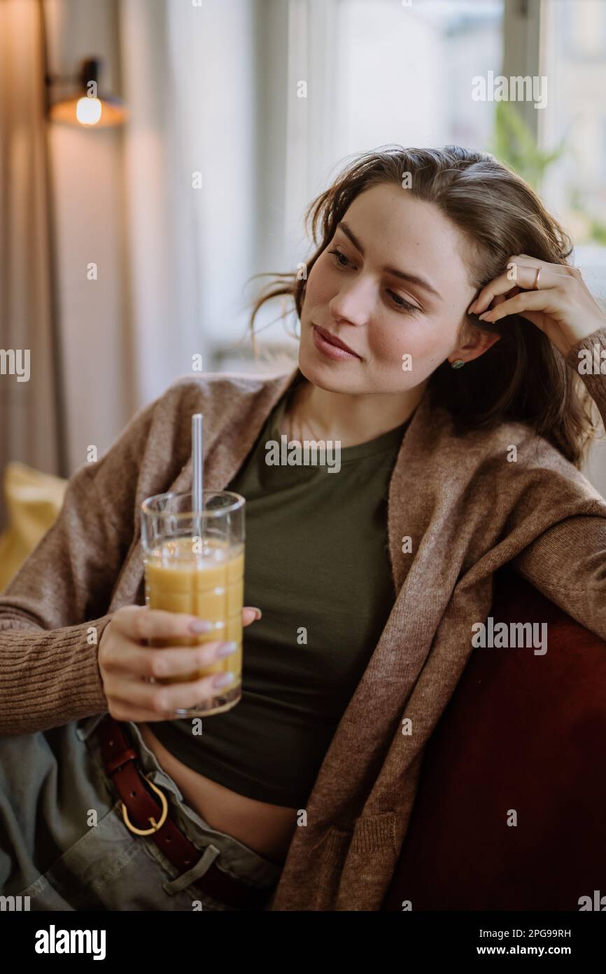Young woman sitting on sofa with drink Stock Photo - Alamy