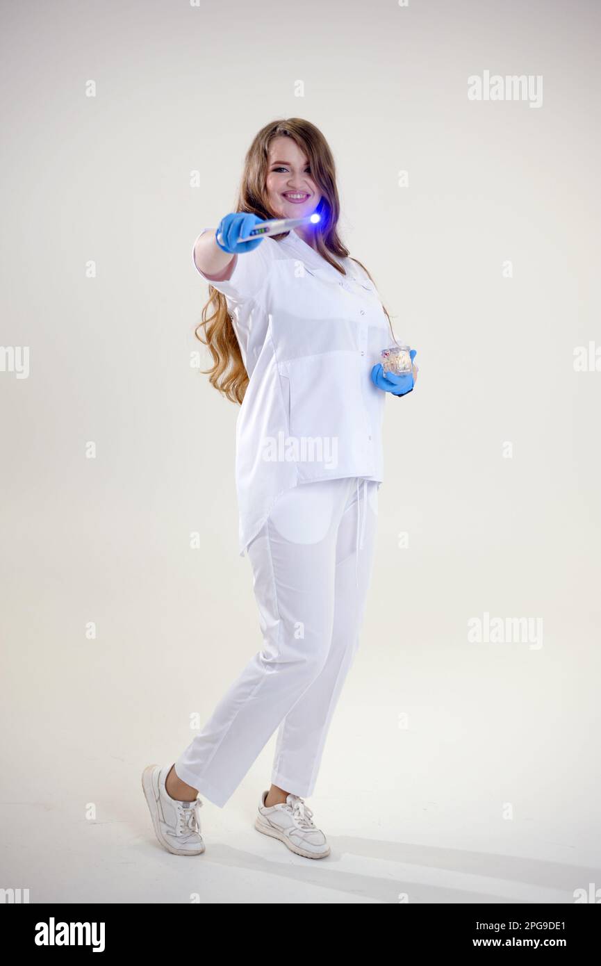 doctor with a magic wand in blue latex gloves. Woman in white medical suit with smart watch with loose hair conjures up a treatment. invents treatments advertisements for tasty supplements medicines Stock Photo