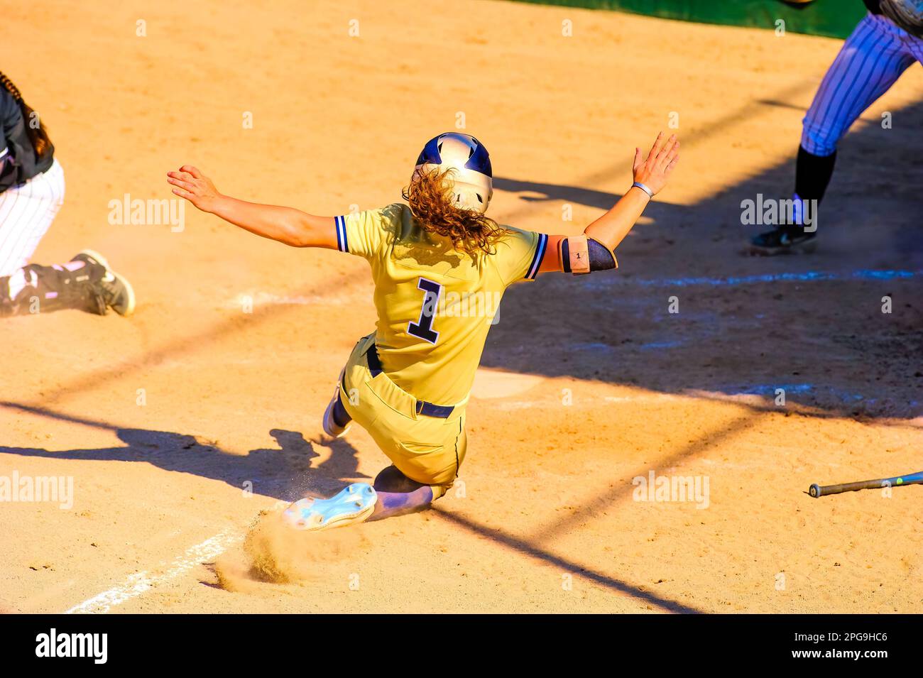 A Female Softball Player Is Sliding Into Home Plate Stock Photo