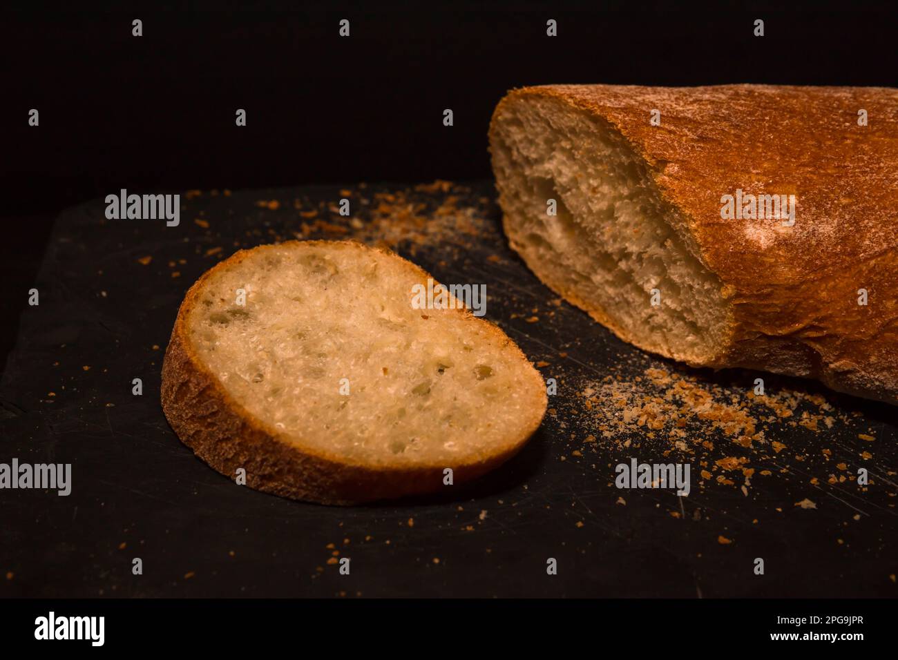 Fresh crispy sliced bread on black board and knife, on a black ...
