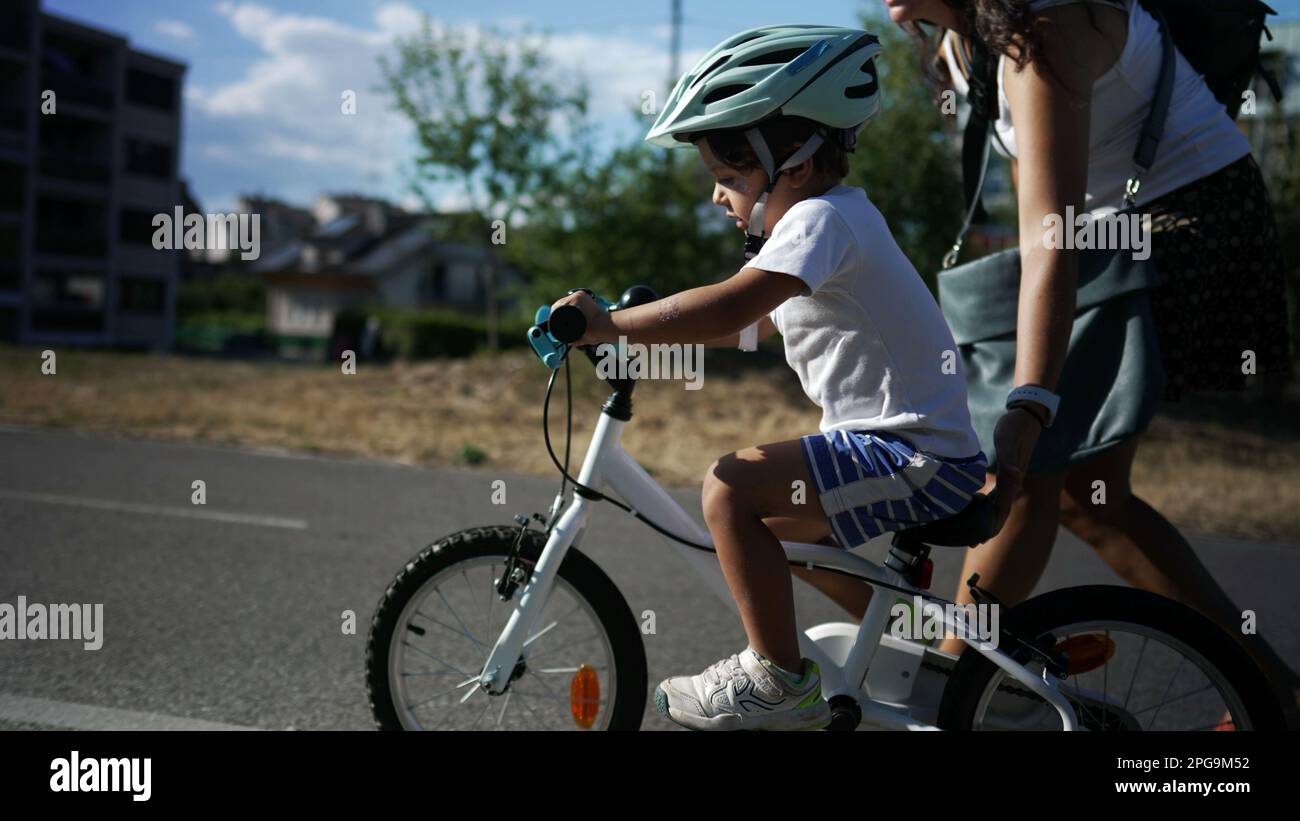 Active little boy learning to ride bicycle outside in sunny day