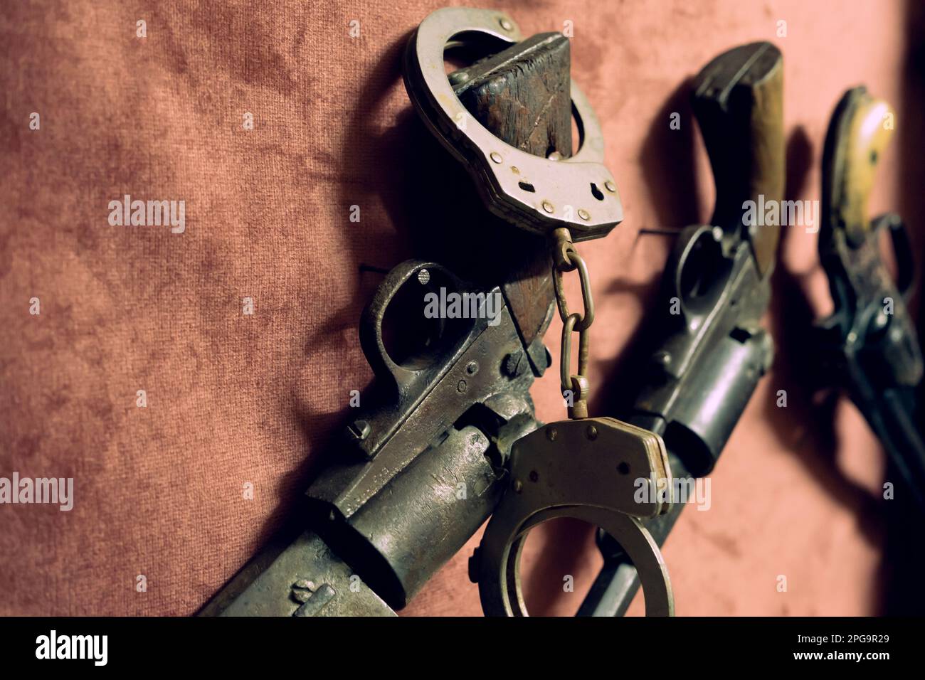 A pair of black handcuffs on top of a black retro pistol. Stock Photo