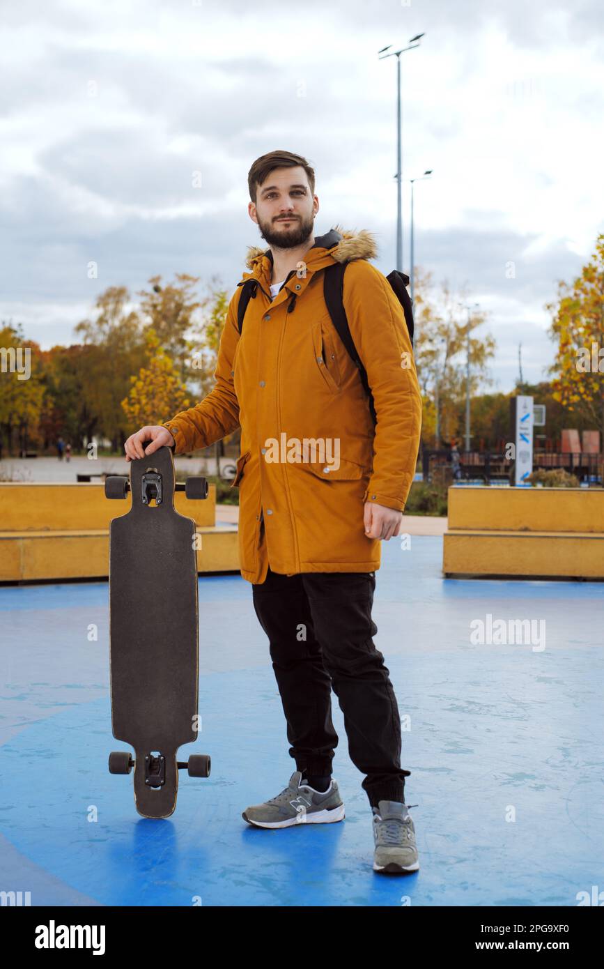 Full-height Portrait of stylish bearded casual young man in a yellow jacket  with a longboard standing at the skating park outdoors Stock Photo - Alamy