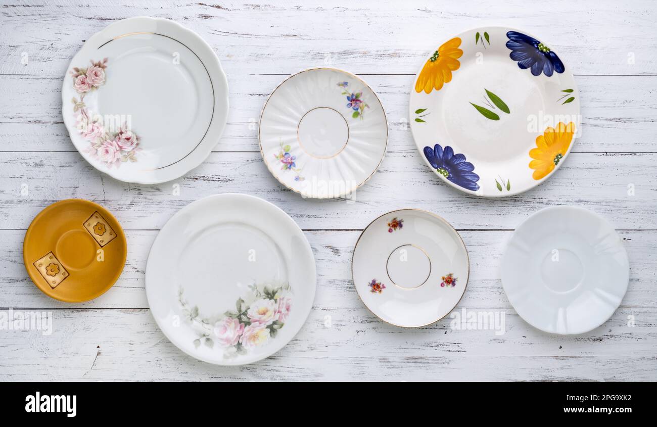 Assorted old vintage ceramic plates over white wooden table. Stock Photo