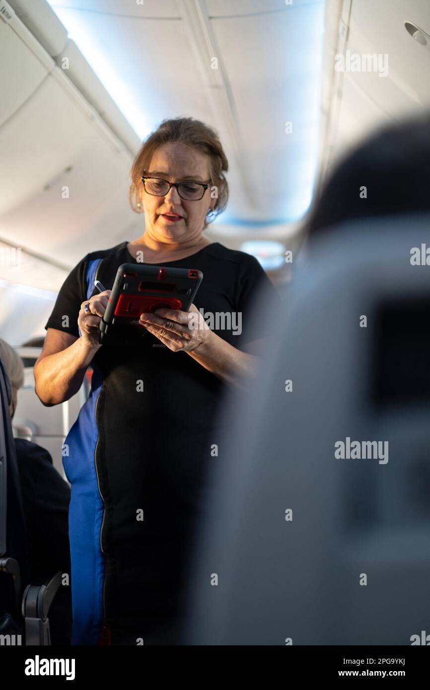 A flight attendant takes drink orders on an airplane. Stock Photo