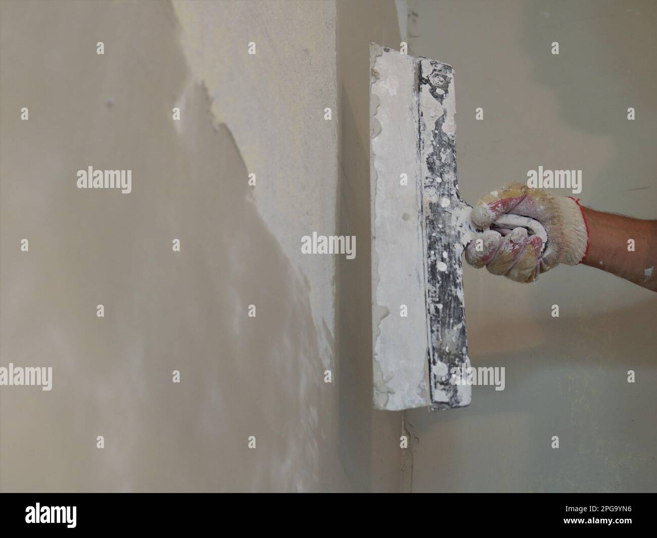 gloved hand of a plasterer holding a wide trowel against a freshly