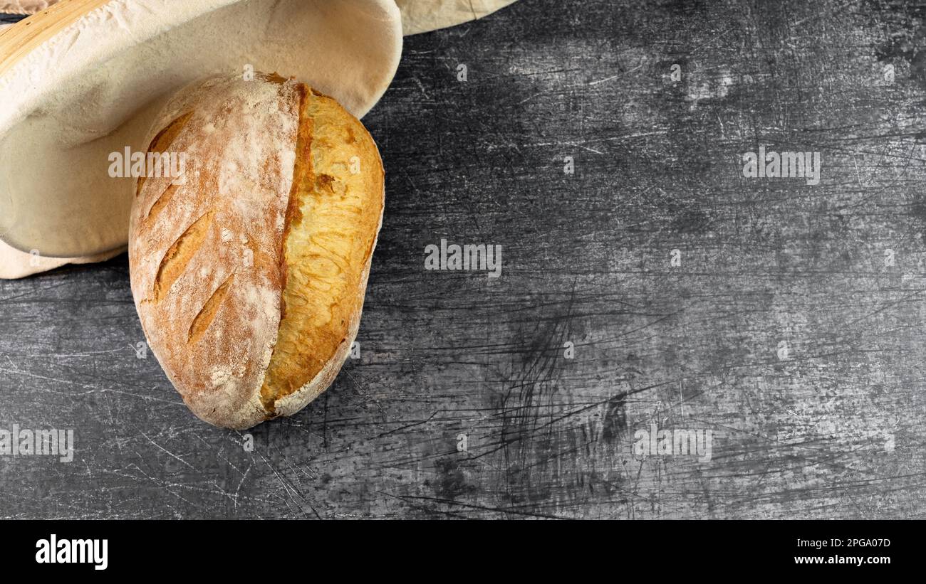 Crusty scored bread on rustic background with a banneton basket. Top view Stock Photo