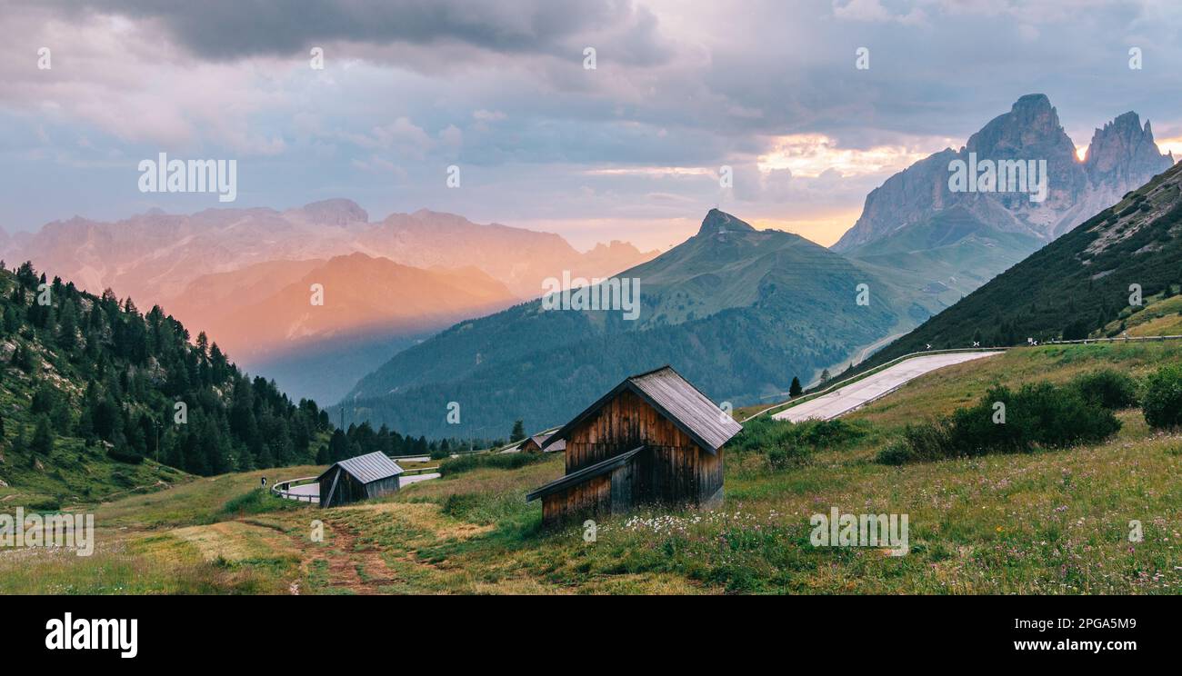 Tranquil alpine landscape of Italian Alps, warm orange golden light of the morning sun illuminates the picturesque wooden houses and verdant meadows o Stock Photo