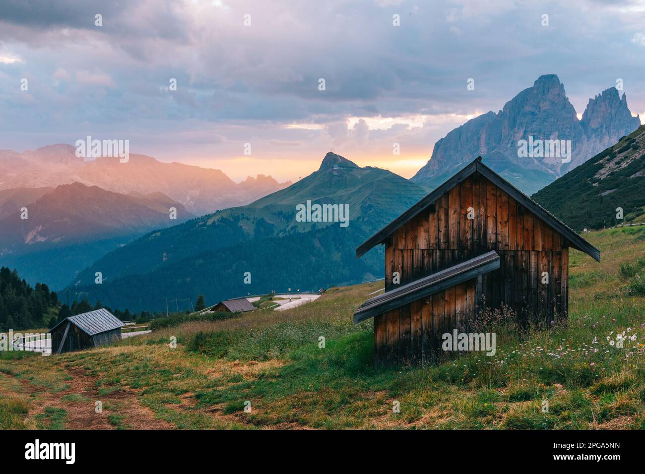 Italian Alps picturesque mountain pass, quiet place of wooden houses surrounded by green meadows. Dawn with warm golden, creating a dreamlike landscap Stock Photo