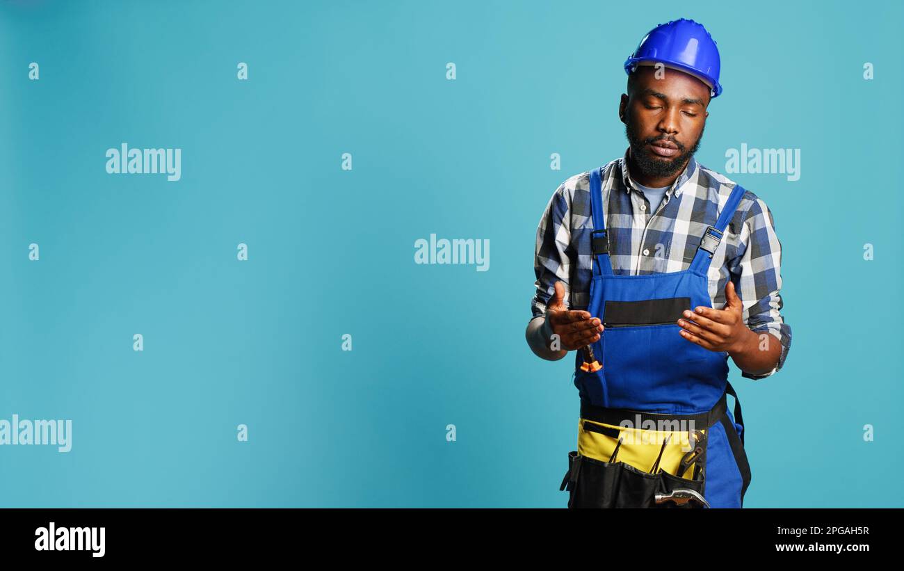 Professional builder almost fainting being wobbly, standing over blue background. Male construction worker feeling light headed with looney tunes cartoons stars on studio camera. Stock Photo